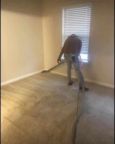 A technician steam-cleaning beige carpet with a wand in an empty bedroom