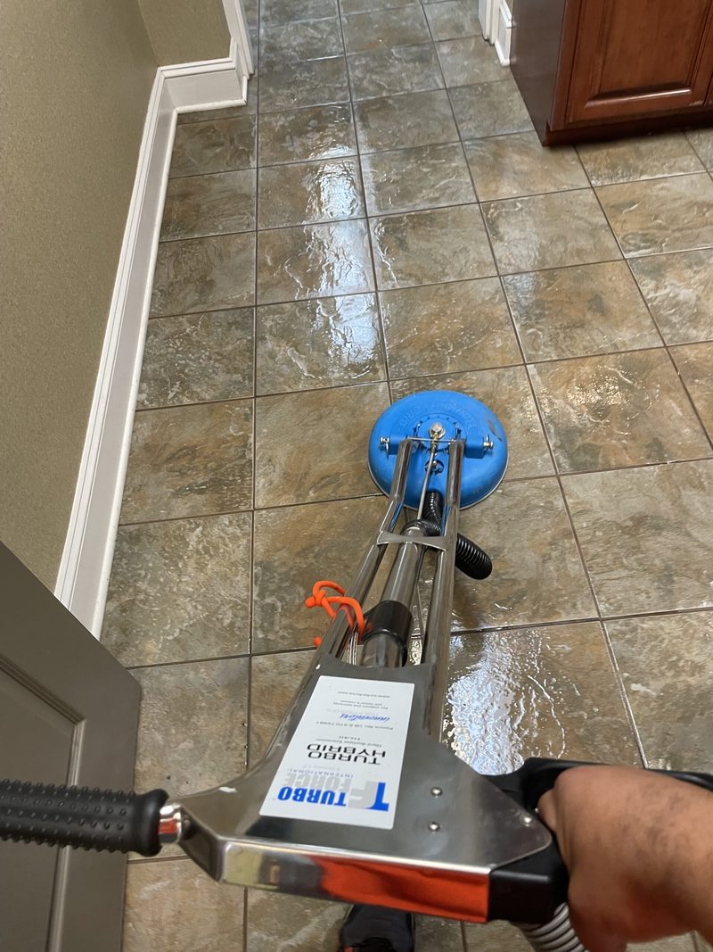 A tile floor being scrubbed with a rotary floor machine, leaving a visibly cleaner wet path