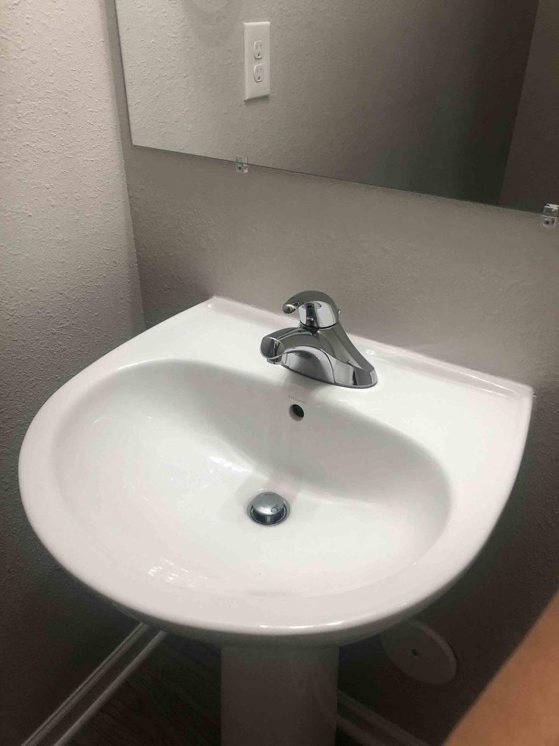 A gleaming white pedestal bathroom sink and chrome faucet after cleaning