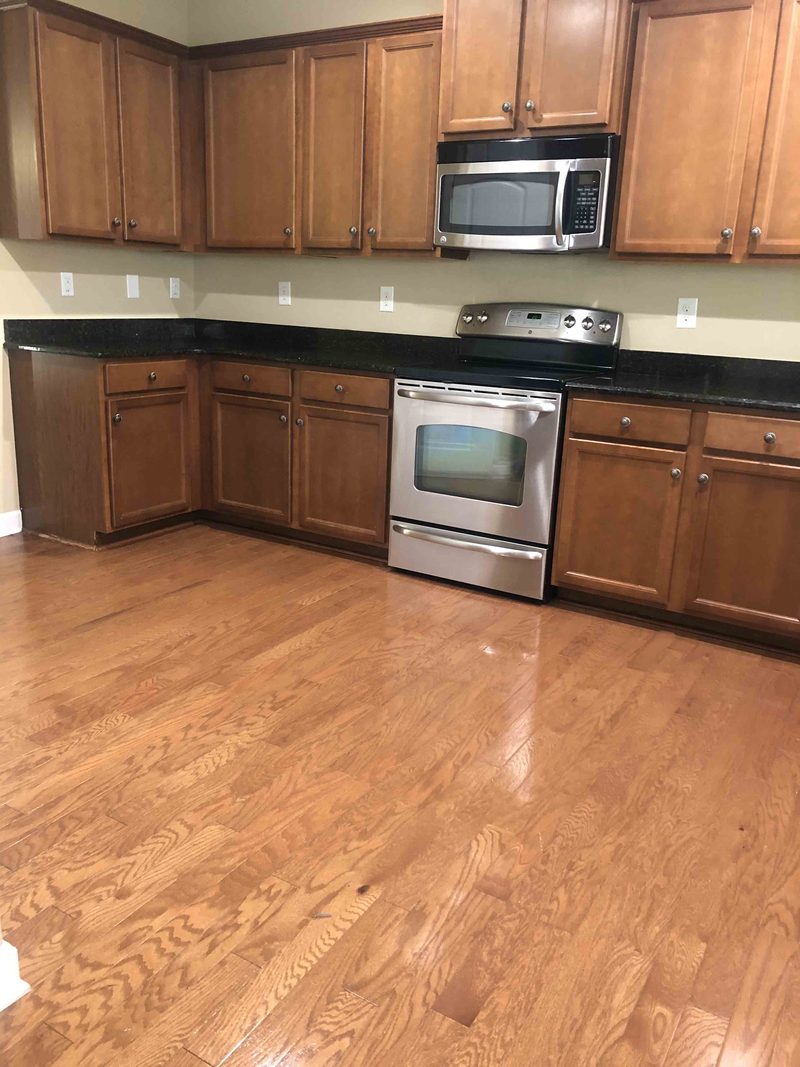 A warm wood-cabinet kitchen with stainless steel appliances and a polished hardwood floor