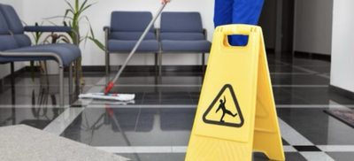 A wet-floor caution sign beside a mop on a freshly cleaned tile floor in an office waiting area