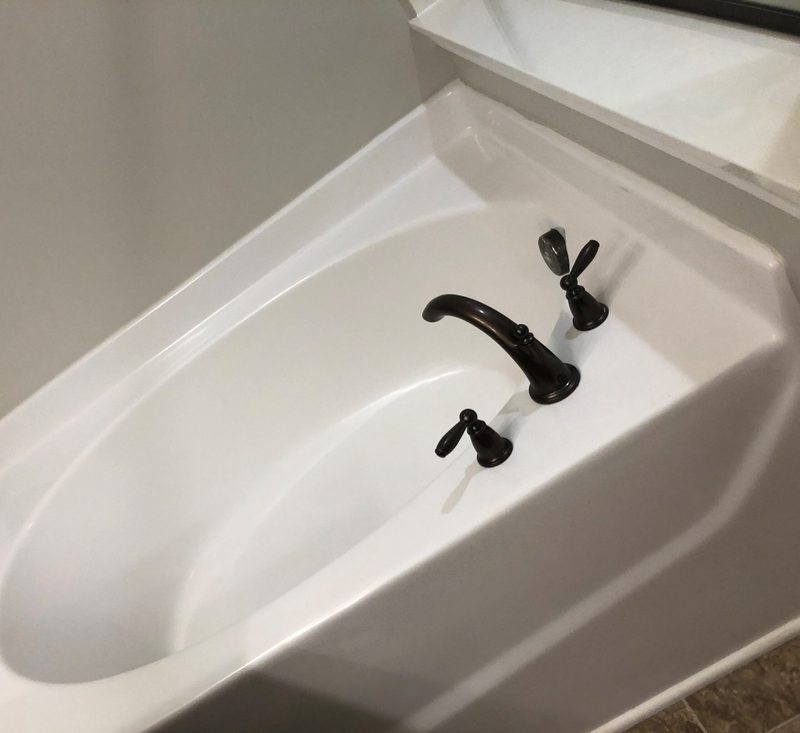 A close-up of a clean white bathtub basin and black fixtures with no visible grime